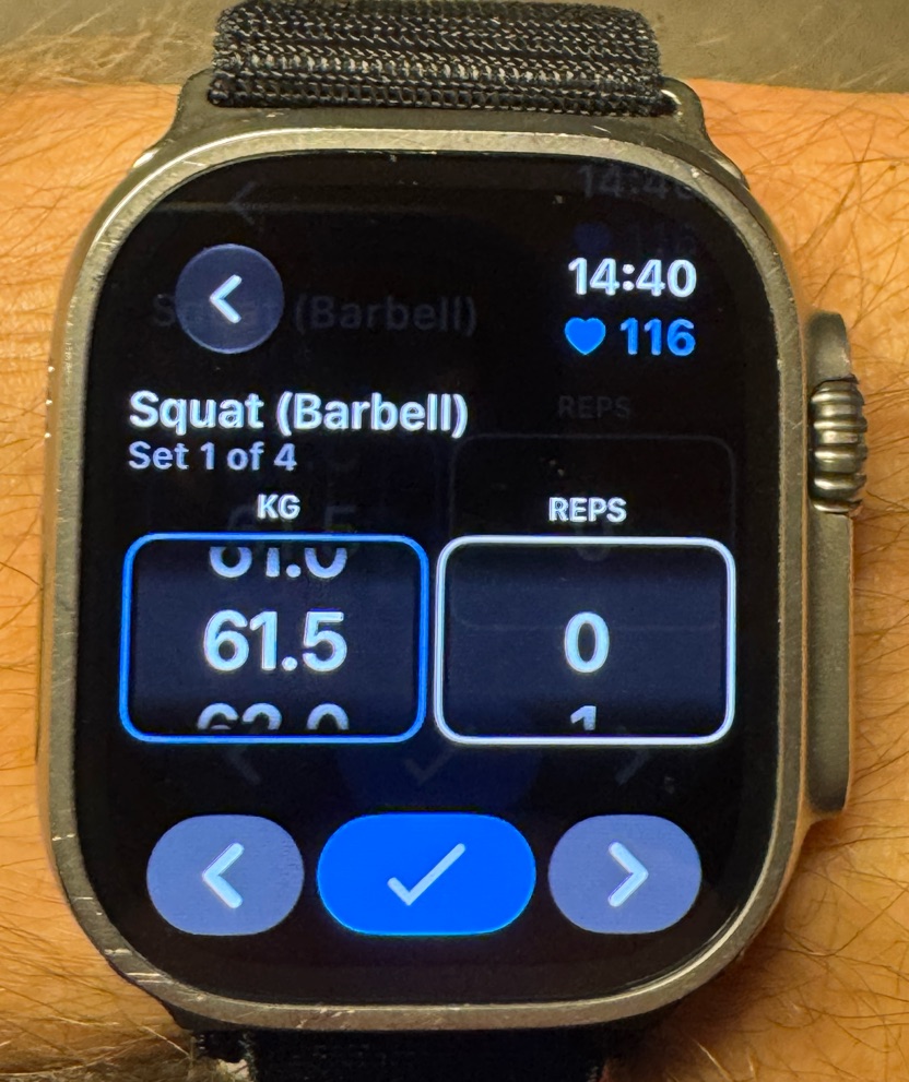 Photo of an Apple Watch Ultra on a wrist showing the Hevy app on Squat (Barbell), set 1 of 4, with a scrolling KG picker at 61.5 and a REPS picker at 0